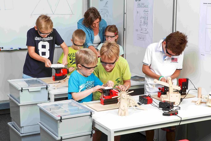 6 Schüler in einem Klassenraum arbeiten mit UNIMAT Grundschulmaschinen an Holzmodellen